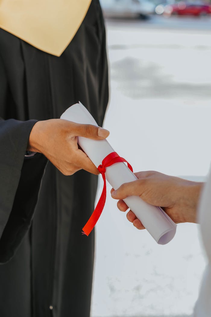 Hands exchanging a graduation diploma wrapped with red ribbon, symbolizing achievement.